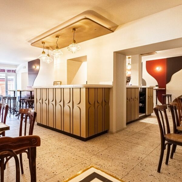 Intérieur du Bistrot de Halles avec comptoir de bar traversant plusieurs salles. Ambiance rétro avec suspentes art déco et motifs en relief peints.