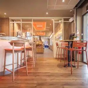 Passage dégagé en perspectives vers le coin presse et tabac PMU.Sur la gauche le retour du comptoir avec chaises hautes et frise en étain, sur la droite une table de bistrot traditionnelle avec quelques chaises hautes