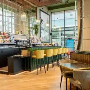 Perspective du bar intégré dans la salle avec tables et banquettes.