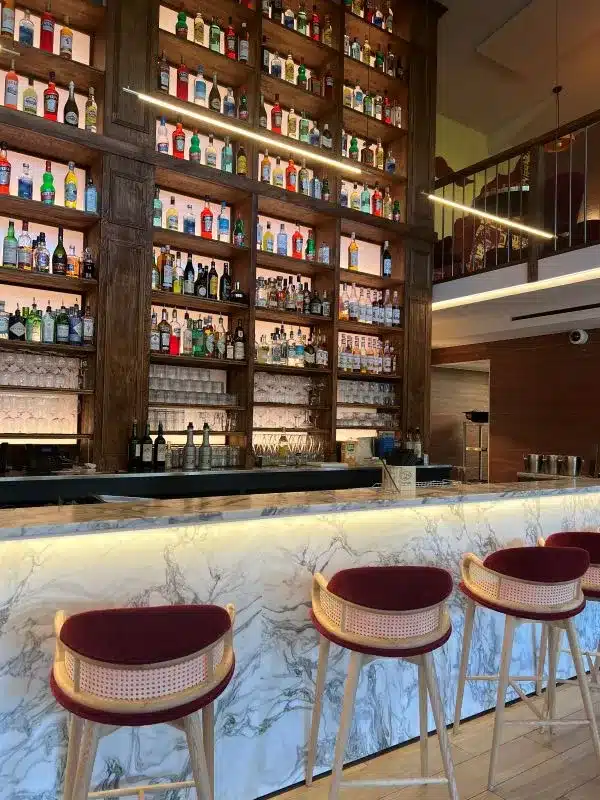 Comptoir en marbre blanc de carrare avec chaises hautes rouge devant et arrière bar toute hauteur avec éclairage LED