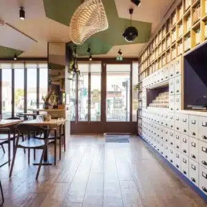 intérieur Coffee shop ACAPELLA avec vue sur porte d'entrée avec rangements muraux style anciens apothicaires sur la droite et espace dégustation sur la gauche.