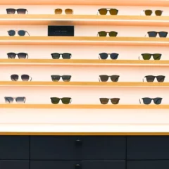 Etageres en bois clair avec LED incrusté suspendues au mur blanc avec plusieurs modèles de lunettes et meuble bas avec tiroirs laqués bleu et poignée noire