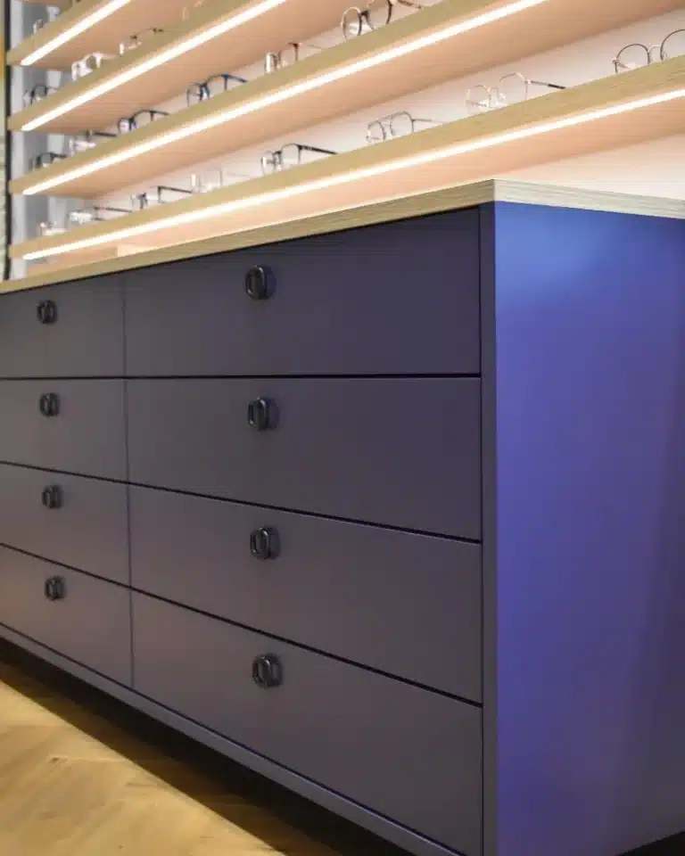 Détail présentoir à lunette pour optique avec étagères bois en partie haute avec LED intégré et meuble bas laqué bleu profond avec tiroirs suspendu en partie basse
