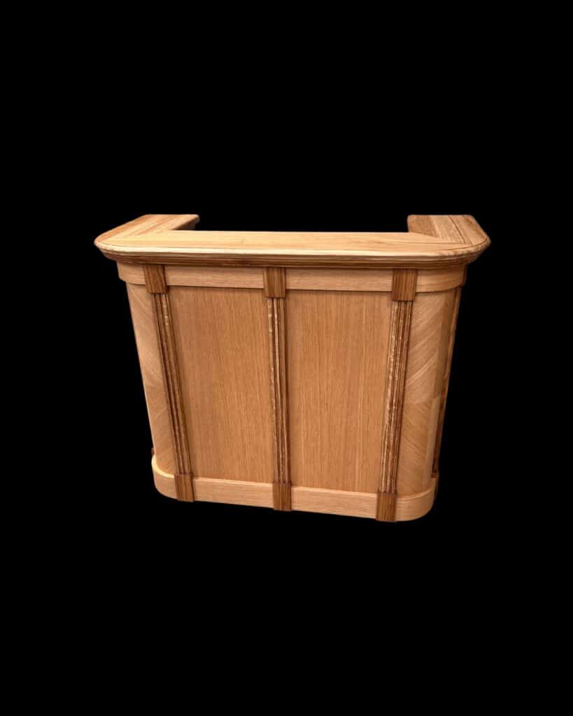 Comptoir compact en chêne massif, modèle Minicomptoir BELFAST, vu de face sur fond noir. Design arrondi avec montants verticaux et finitions artisanales ARANDA-MAS.