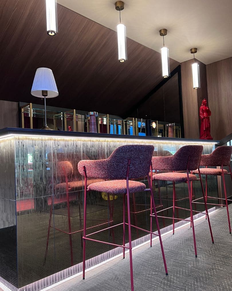 Façade de bar en miroir texturé rétroéclairé avec tabourets rouges et dessus en granit noir.