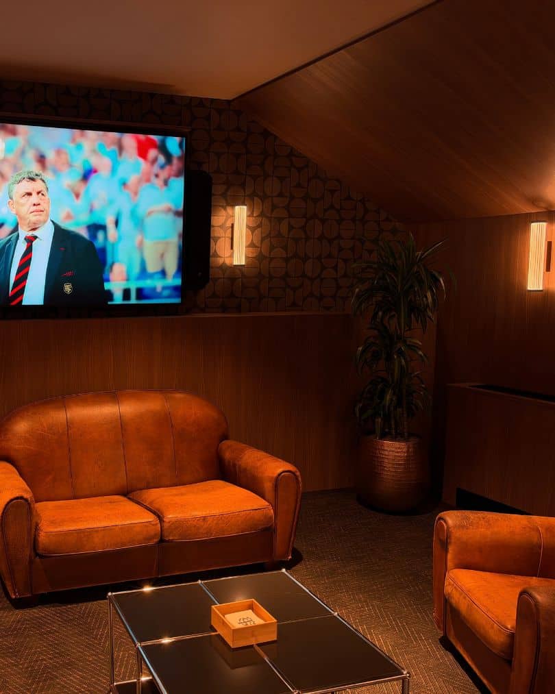 Salon VIP avec canapé et fauteuil club en cuir, boiseries et télévision intégrée au Stade Toulousain.